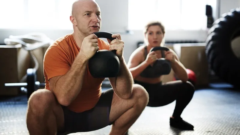 Man and woman training with kettlebells together in a gym